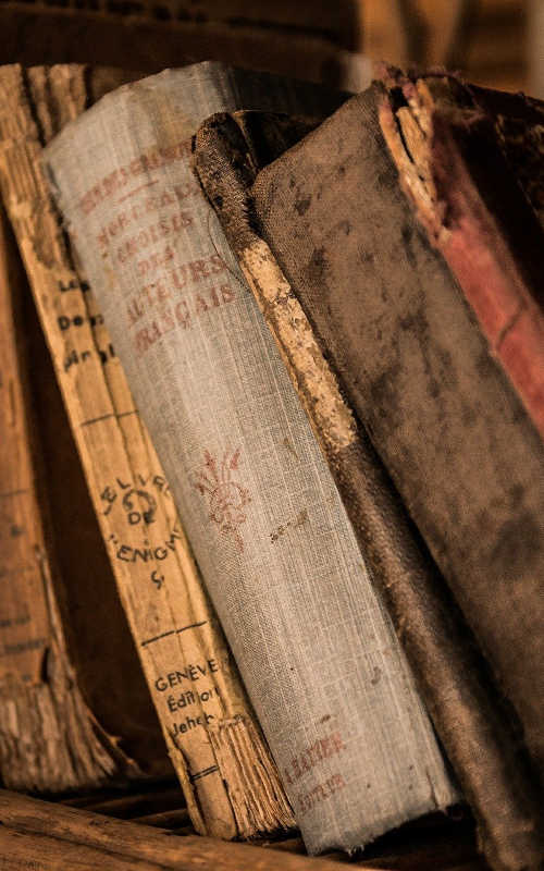 close up of old books leaning over on a shelf